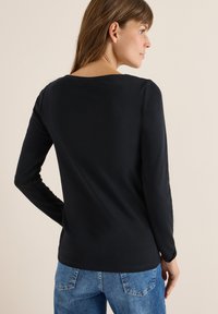 Zwarte langemouwen shirt van zacht materiaal, met een ronde halslijn en een getailleerd ontwerp, gecombineerd met blauwe denim jeans.