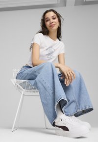 Hvid kortærmet t-shirt med grafisk print, parret med lyseblå brede denim jeans og hvide sneakers med lilla accenter.