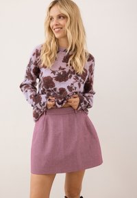 Gebreide trui in lavendel met een donker bloempatroon; gecombineerd met een strakke, lichtplum kleurige rok met plooien en een gestructureerde weefsel.