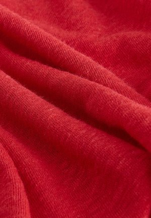 Röd stickad tyg med en mjuk, fluffig textur, som visar veck och subtila variationer i nyans och täthet genom hela materialet.