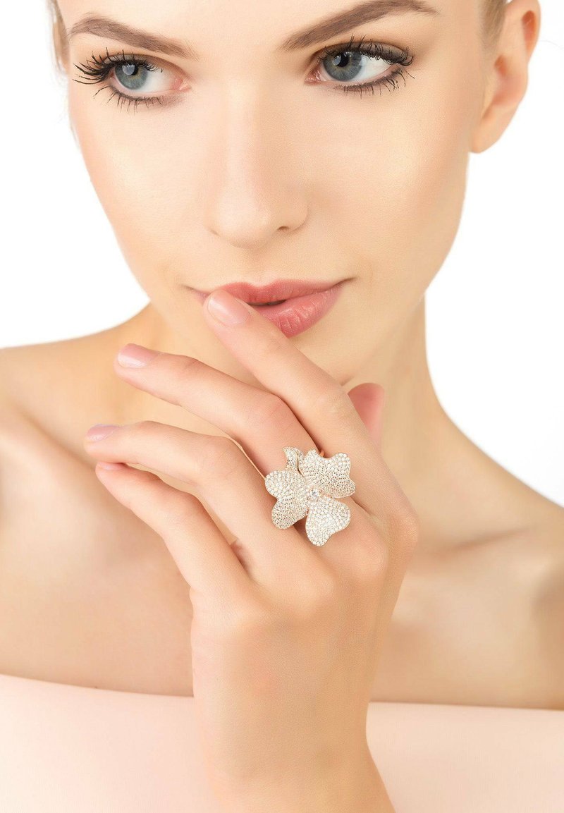 Rhinestone flower ring with three petal design, silver accents, and a central gemstone, showcased on a hand against a neutral background.