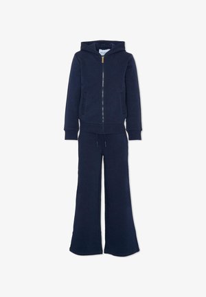 Felpa blu navy con zip frontale e pantaloni a gamba larga abbinati, dotati di tasche e vita con cordino, esposti su sfondo bianco.