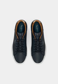 Par crnih vezanih tenisica s bijelim potplatima i smešim unutrašnjim oblogama, viđeno od gore na beloj pozadini.