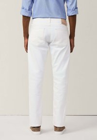 Pantaloni in denim bianco con un design aderente, dotati di due tasche posteriori e una toppa in pelle in vita. Indossati con una camicia blu chiaro.