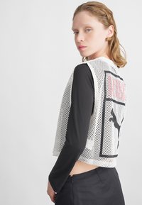 Witte mesh crop top met zwart grafisch ontwerp en een zwart lang mouwtjes shirt, met een rits aan de achterkant en een gladde textuur.