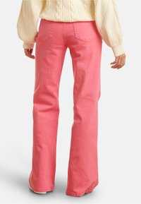 Pink flared jeans made of cotton with a smooth texture. Features two back pockets and a mid-rise waist.