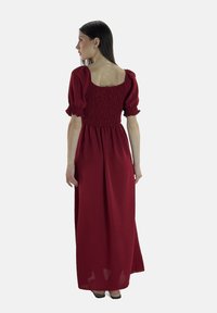 Rotes Maxikleid mit gerafftem Oberteil und kurzen Puffärmeln. Fließender Stoff, quadratischer Rücken, weiche Textur und knöchellanges Design.