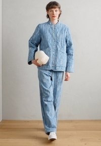 Giacca trapuntata azzurro chiaro e pantaloni abbinati, con una sottile texture marmorizzata, abbinati a sneakers bianche e a una scultura bianca rotonda.