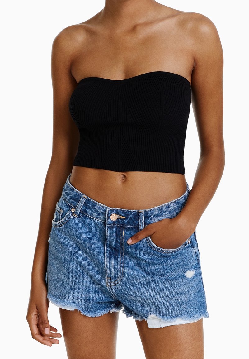 Top bustier negro con textura acanalada y escote corazón, combinado con pantalones cortos de mezclilla con dobladillo deshilachado y detalles desgastados.
