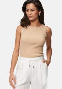 Top sans manches beige à côtes avec des bords festonn�és. Fabriqué en tissu lisse, design ajusté. Assorti à un pantalon blanc taille haute.
