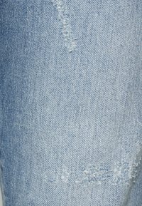 Tela de mezclilla azul claro con un acabado desgastado. Presenta bordes deshilachados y un desvanecimiento irregular, lo que le da una apariencia texturizada y envejecida.