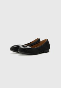 Black suede flats with a rounded toe, featuring a large metallic buckle accent on the front and a low heel for comfort.