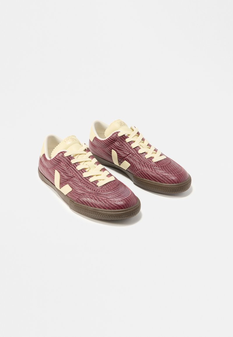 Ζευγάρι χαμηλών αθλητικών παπουτσιών με υφή μπορντό επάνω μέρος, κρεμ κορδόνια, γλώσσες και λεπτομέρειες στη φτέρνα, καθώς και καφέ λαστιχένιες σόλες σε λευκό φόντο.