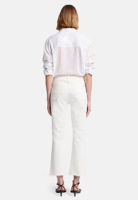 Witte overhemden met opgerolde mouwen, gecombineerd met off-white flare jeans met rafelige zoom en achterzakken. Model wordt van achteren getoond.
