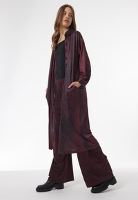 Bordeaux lange blouse met een geruit patroon, gecombineerd met bijpassende wijde broek en zwarte enkelboots; zachte textuur en knoopdetails.