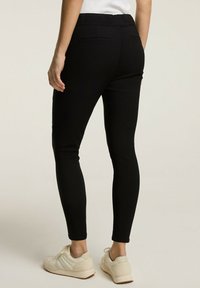 Czarne legginsy o dopasowanym kroju, z elastycznym pasem i kieszeniami z tyłu. Materiał wygląda na gładki i dobrze przylegający do ciała.