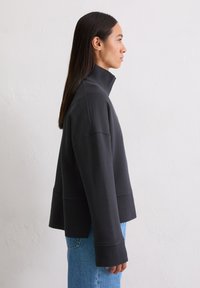 Czarny sweter z wysokim kołnierzem o luźnym kroju, z ribbami na mankietach oraz wyraźnym dolnym wykończeniem. Miękki materiał i minimalistyczny design.