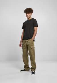 T-shirt noire à manches courtes assortie à un pantalon cargo vert olive avec poches latérales, complété par des baskets noires. Fond uni.