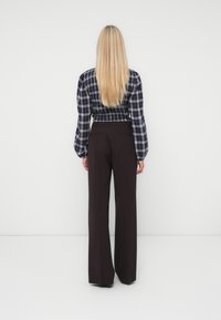 Chemisier à carreaux avec des manches ballon, taille cintrée, associé à un pantalon taille haute à jambes larges de couleur marron foncé. Textures de tissu lisses visibles.