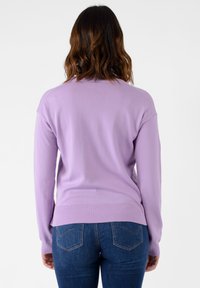 Maglione a maglia lilla con scollatura rotonda, polsini e orlo a costine. Abbinato a jeans blu con dettagli di cucitura sulle tasche posteriori.