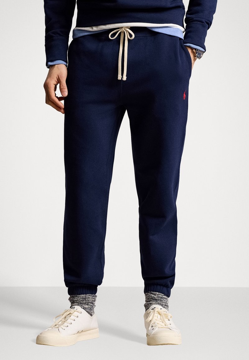 Marinkbluea sweatpants i mjukt material, med dragsko i midjan, ribbade anklar och en liten röd logotyp på vänster sida.