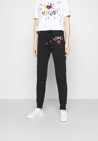 Black sweatpants with 'LOVE!' and a heart design in red glitter, featuring an elastic waistband and cuffs. Paired with a white graphic tee.