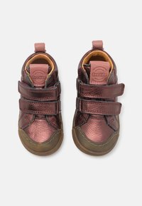 Chaussures pour tout-petit de couleur bronze avec une finition brillante, dotées de deux bandes velcro, d'un bout rond et d'une semelle en caoutchouc marron. Doublées de jaune.