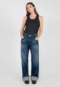 Jeans de denim azul de pierna ancha con puños doblados, combinados con una camiseta sin mangas negra. Presentan costuras clásicas y un ajuste relajado.
