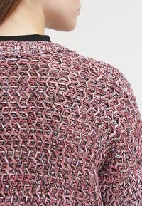 Pletený svetr s texturovaným vzorem prolínajících se šestiúhelníků v odstínech růžové, šedé a černé, s kontrastním černým výstřihem.