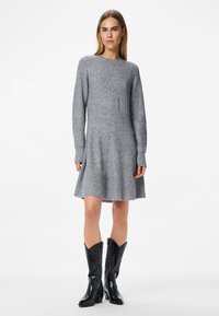 Γκρίζα πλεκτή φόρμα με μακριά μανίκια και φουσκωτό φούστα, συνδυασμένη με μαύρες δερμάτινες καουμπόικες μπότες με διακοσμητική ραφή.