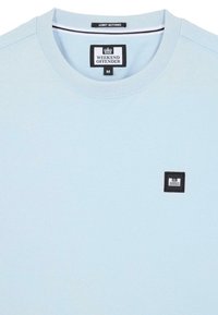 Lichtblauwe katoenen T-shirt met ronde hals, voorzien van een rechthoekig zwart label met witte tekst in de linkerbovenhoek.