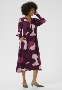 Lila och rosa mönstrad midi-klänning med långa ärmar, v-ringning och fickor; bärs med svart och vit randig slingback-sko.