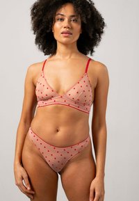 Wäsche Set aus leichtem nacktfarbenem Mesh mit roten Herzmustern. Der Bralette hat verstellbare Träger und eine Dreiecksform; passende hochgeschnittene Panty.