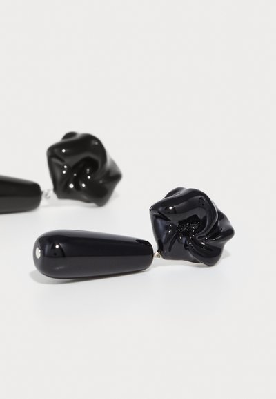 Schwarze Ohrringe mit einem verdrehten, floralen Design und glänzender Oberfläche in tropfenförmiger Form. Hergestellt aus glänzendem Material mit silbernen Beschlägen.