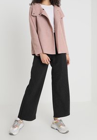 Ljusrosa skräddarsydd jacka med hög krage och tryckknappar, kombinerad med svarta byxor med smalrand och gråvita träningsskor.