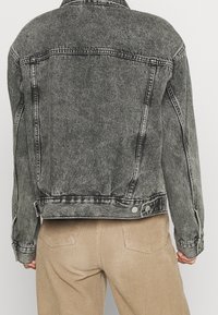 Giacca di jeans in nero sbiadito con cuciture visibili, colletto classico e dettagli con bottoni. La vista posteriore mostra una vestibilità strutturata e linee pulite.