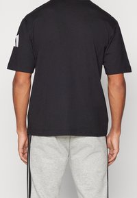 Černé bavlněné tričko s krátkým rukávem, se znakem na levém rukávu. Ve spojení se světle šedými tepláky s černými postranními pruhy.