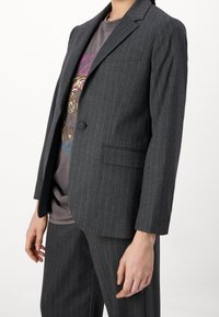 Grå kostymjacka med randig struktur, enkel knappstängning, spetsiga slag och sidficka. Bärs över en grafik-t-shirt.