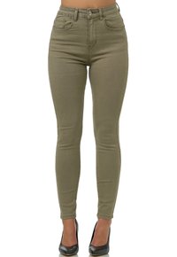 Jeans skinny de tiro alto en verde oliva con diseño de cinco bolsillos, tela texturada y detalles de costura sutiles, combinados con tacones altos negros.