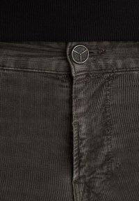 Pantaloni in corduroy grigio con una superficie testurizzata, dotati di chiusura a bottone con logo metallico. Design semplice e funzionale.