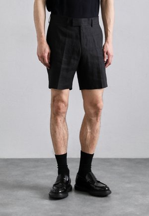 Zwarte linnen shorts met een getailleerde pasvorm, zijzakken en een gladde stoftextuur, gecombineerd met zwarte leren loafers en crew-sokken.