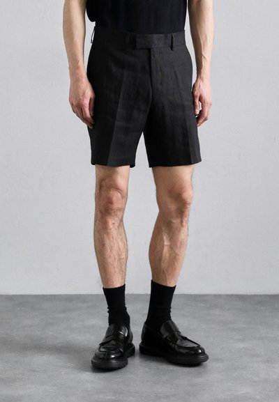 Sorte linnedestoffer med en skræddersyet pasform, sidelommer og en glat stofstruktur, parret med sorte læder loafers og crew socks.