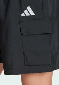 Black shorts with a large side cargo pocket. Features a reflective silver Adidas logo on the front, smooth fabric texture, and clean stitching.