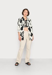 Camisa com padrão abstrato em preto e branco, top preto cropped, calças largas bege e sandálias pretas. Conjunto simples e casual com texturas sobrepostas.