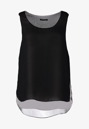 Top negro sin mangas con un diseño fluido, superpuesto sobre una base blanca, combinado con jeans skinny blancos y botas de tobillo negras.