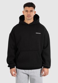 Sweat à capuche noir au fit décontracté avec une poche avant et un logo blanc sur la poitrine. Texture douce avec des poignets et un ourlet en côtes.