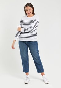 Hvid langærmet skjorte med marineblå vandrette striber, rund halsudskæring og et diskret logo. Sammen med lige ben blå denim jeans og hvide sneakers.