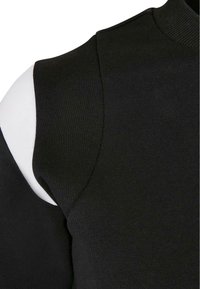 Suéter negro de punto con cuello alto, que presenta un distintivo diseño de hombros descubiertos. Textura suave con bordes acanalados.