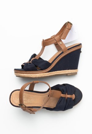Navy blue wedge sandals with tan leather ankle straps, knotted fabric front, and jute-wrapped platform soles on white background.