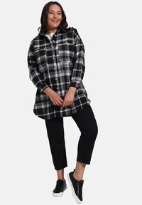 Chemise en flanelle à carreaux noir et blanc avec un devant à boutons, des manches longues et une poche poitrine, associée à un pantalon noir court et des baskets.